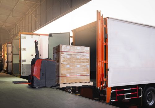 electric-forklift-loading-package-boxes-into-container-trucks-parked-loading-dock-warehouse