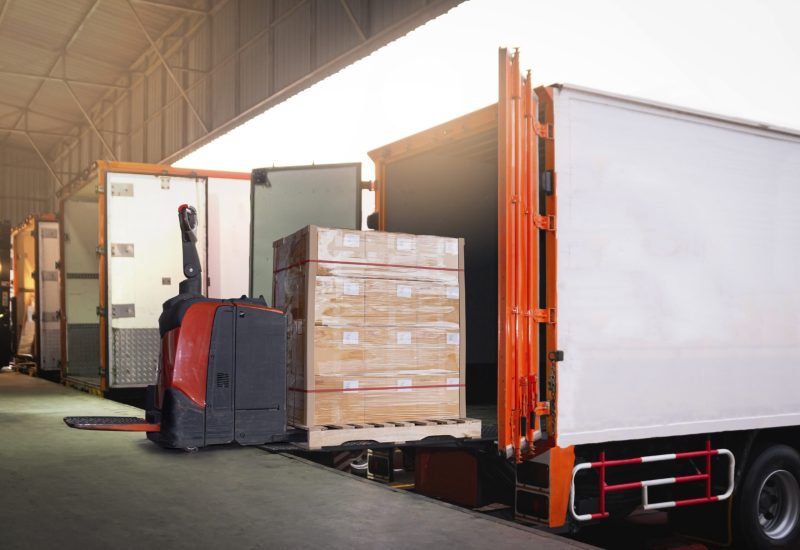 electric-forklift-loading-package-boxes-into-container-trucks-parked-loading-dock-warehouse
